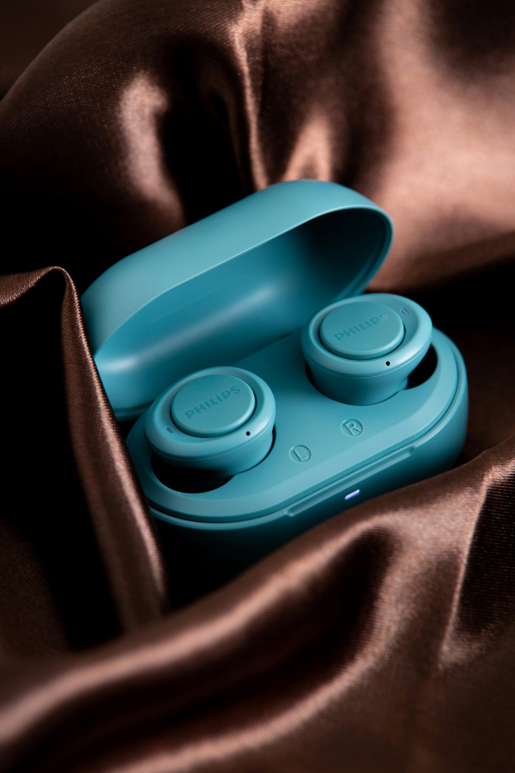 pexels photo 13939463 13939463 A close-up shot of wireless earbuds in a teal case set against luxurious satin fabric.