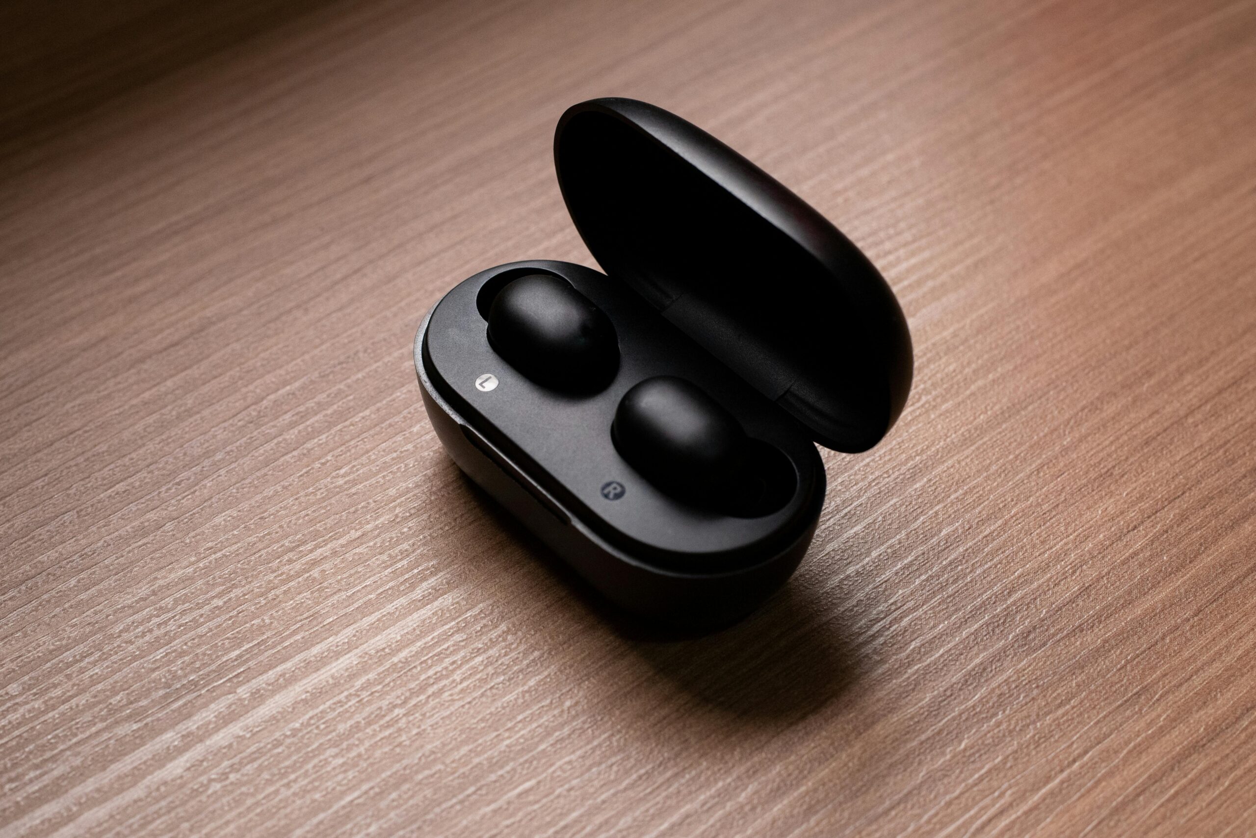 pexels photo 7247777 7247777 Stylish black wireless earbuds displayed in an open charging case atop a wooden table.